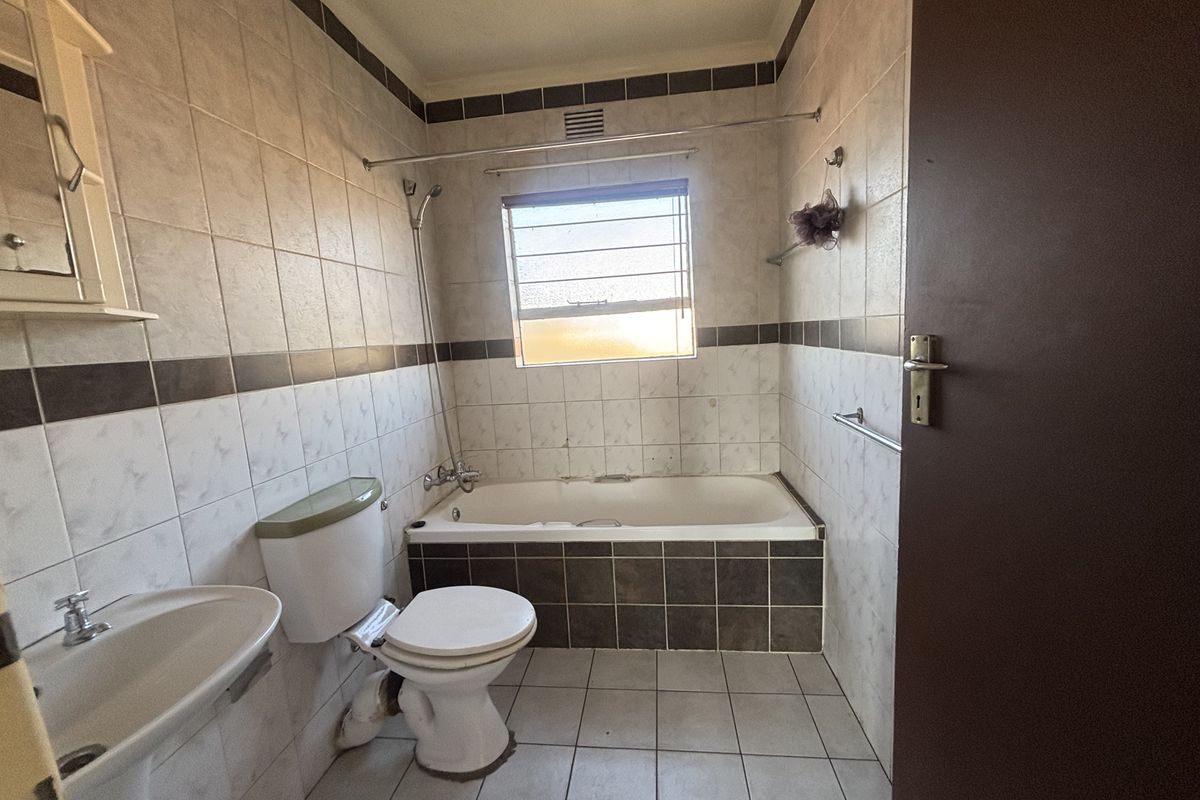 A functional bathroom featuring a bathtub with shower mixer, pedestal basin, and toilet, finished with neutral wall and floor tiling.