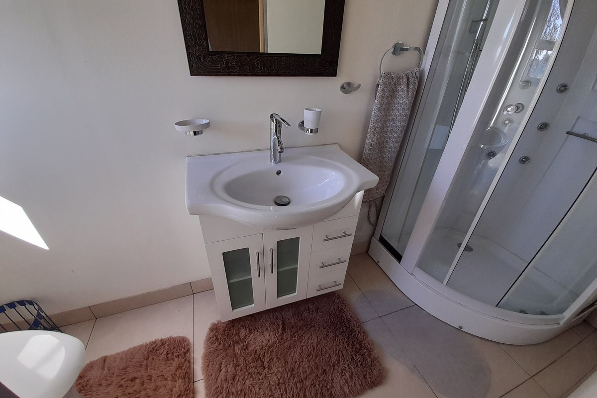 A functional bathroom featuring a modern vanity with a ceramic basin, chrome mixer tap, and a corner shower enclosure with tiled flooring.