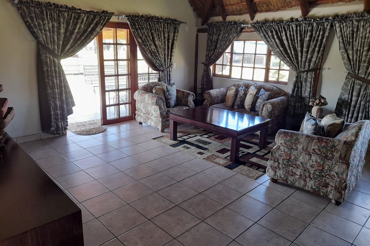 Spacious living room featuring a traditional thatched roof with exposed timber rafters, ceramic tiled flooring, and direct access to an outdoor patio area.