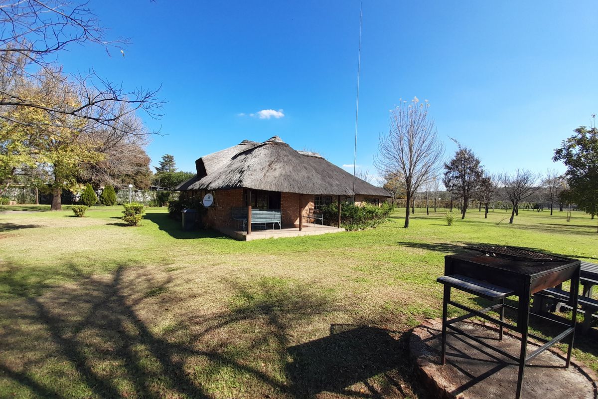 A rear view of a brick townhouse featuring a traditional thatched roof and a covered patio area set within a spacious garden.
