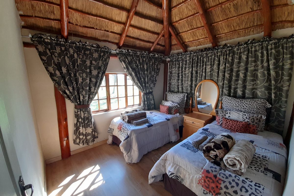 A bedroom featuring a traditional thatched roof with exposed timber rafters and support posts, complemented by laminate flooring and natural light.