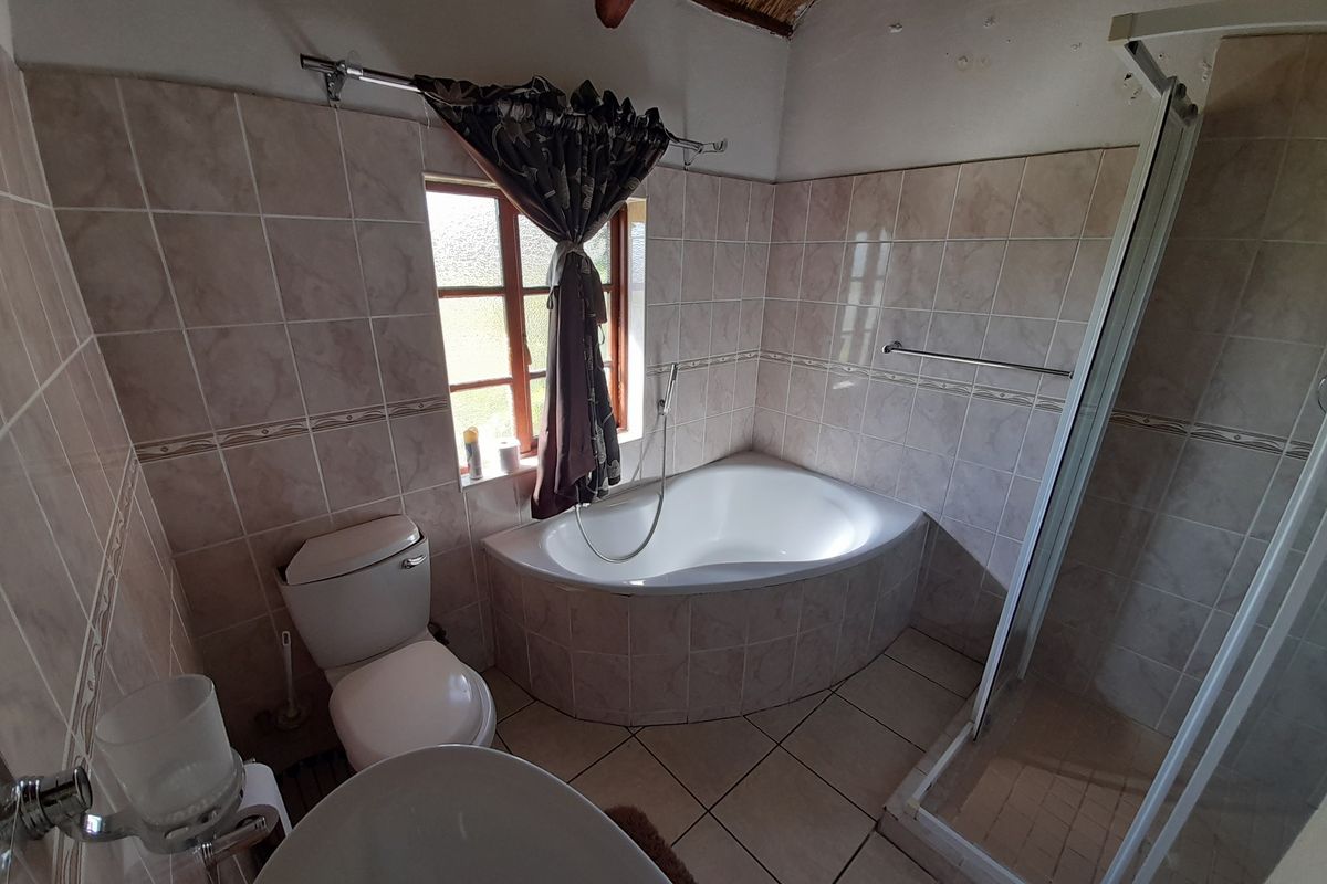 A functional bathroom featuring a corner bathtub, separate shower enclosure, tiled finishes, and exposed timber rafters under a pitched ceiling.