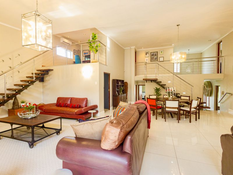 Spacious open-plan living and dining area featuring a modern floating staircase, mezzanine level, and polished porcelain flooring throughout.