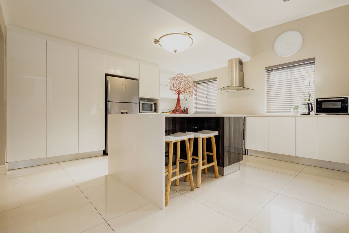 Modern kitchen featuring high-gloss white cabinetry, a central island with dark wood accents, stainless steel extractor fan, and polished floor tiles.