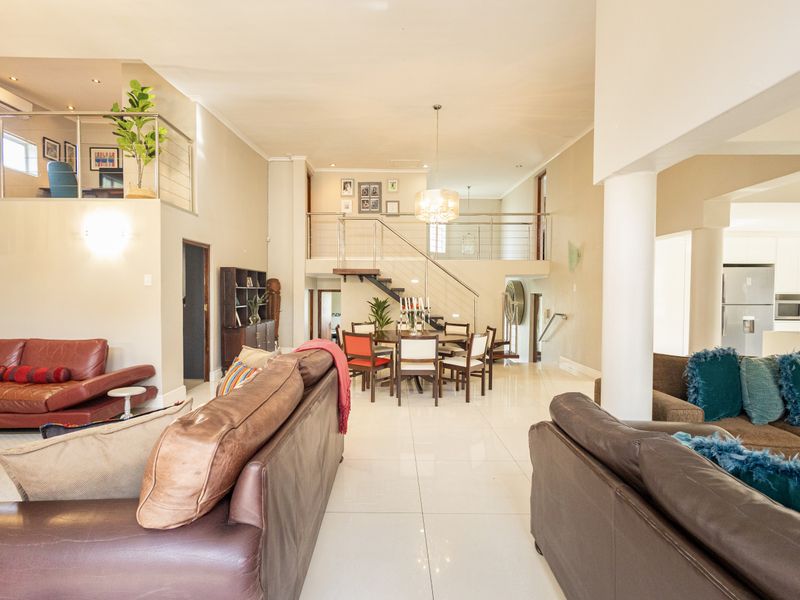 Spacious open-plan living and dining area featuring a split-level mezzanine, modern tiled flooring, and a contemporary staircase with stainless steel balustrades.
