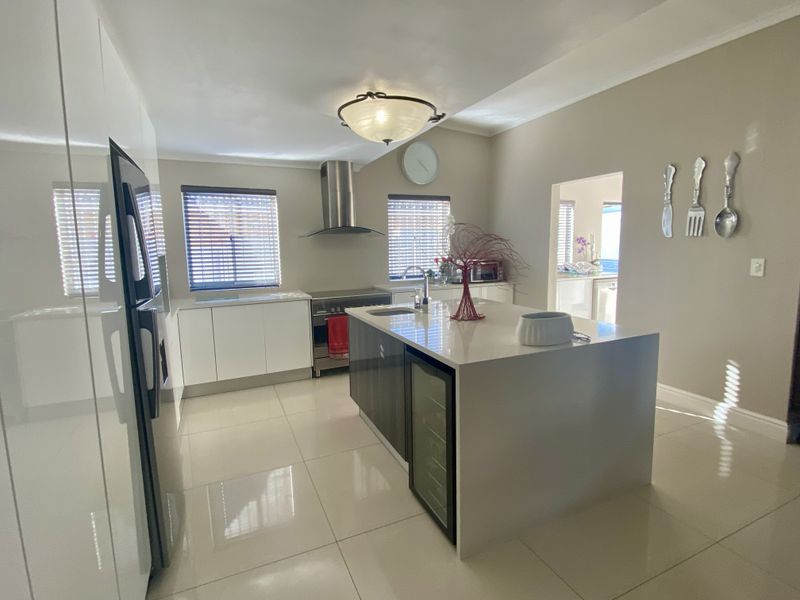 Modern kitchen featuring a central island with a wine cooler, stainless steel extractor fan, built-in oven, and sleek white cabinetry with tiled flooring.