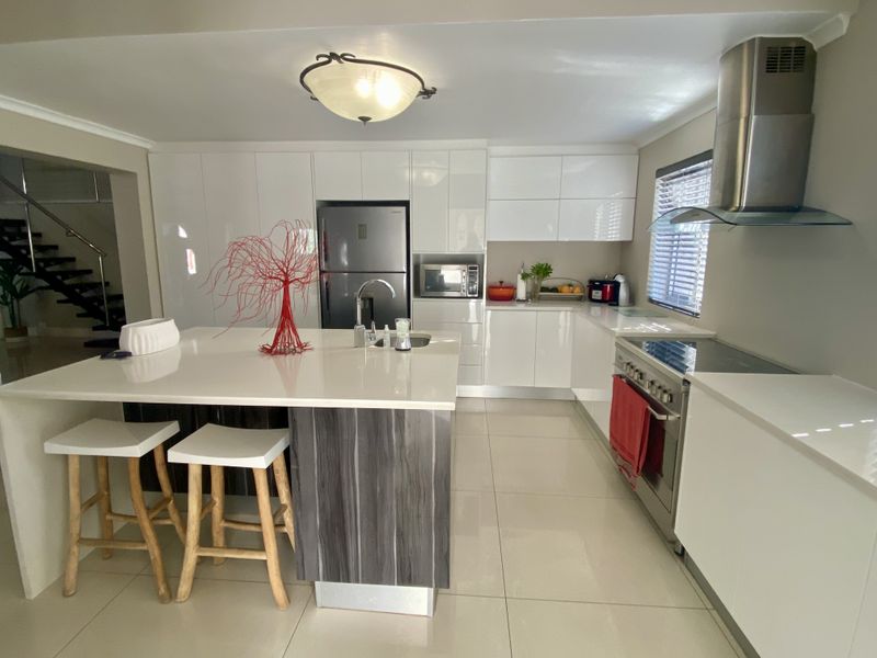 Modern kitchen featuring high-gloss white cabinetry, a central island with quartz countertops, stainless steel appliances, and sleek porcelain floor tiles.