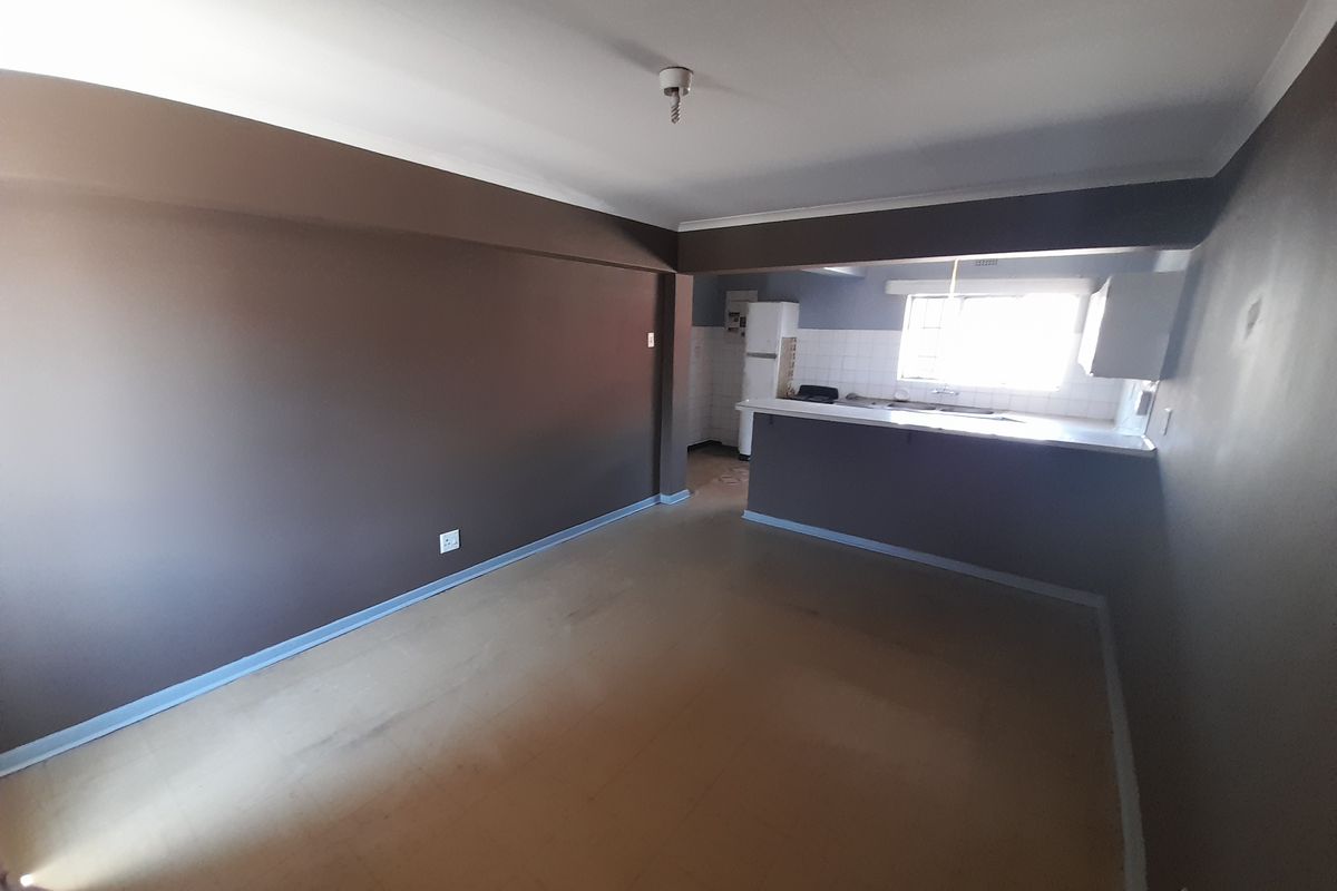 An empty open-plan living and kitchen area featuring dark painted walls, vinyl flooring, and a functional kitchen counter with a sink.