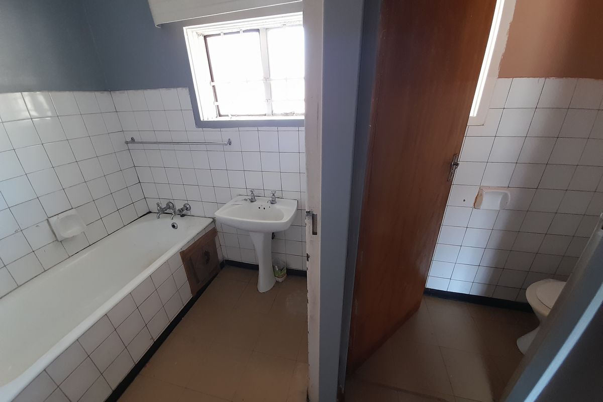 A dated bathroom featuring a bathtub, pedestal basin, and separate toilet area with original wall and floor tiling.