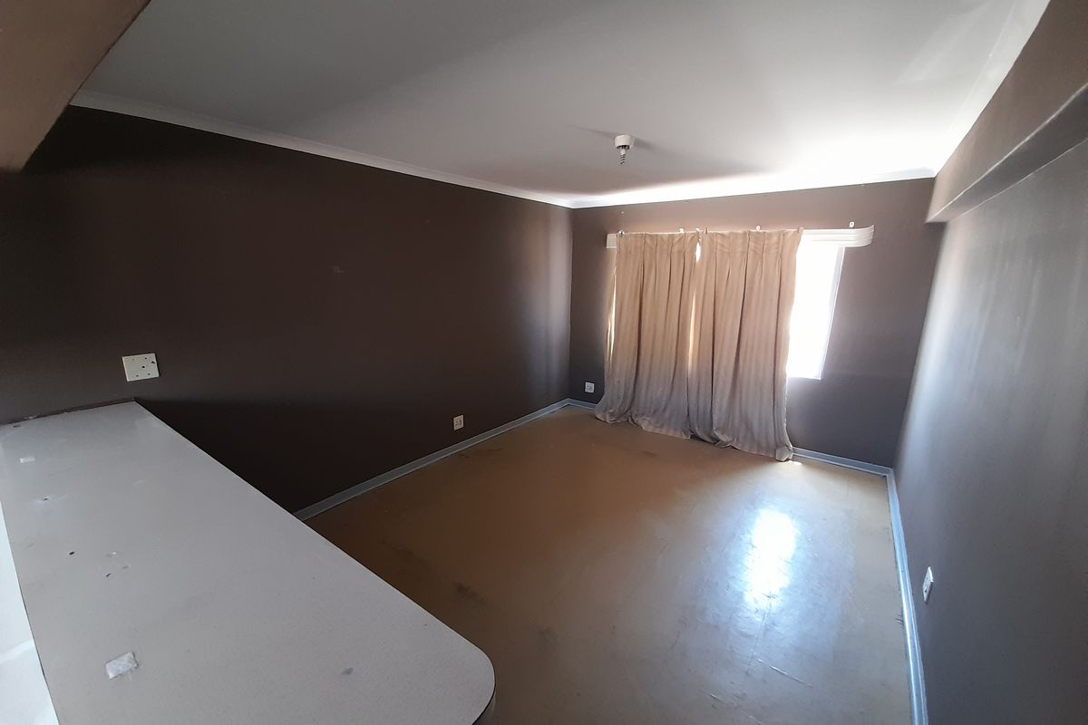 An empty bedroom featuring dark painted walls, a built-in desk area, and window curtains.