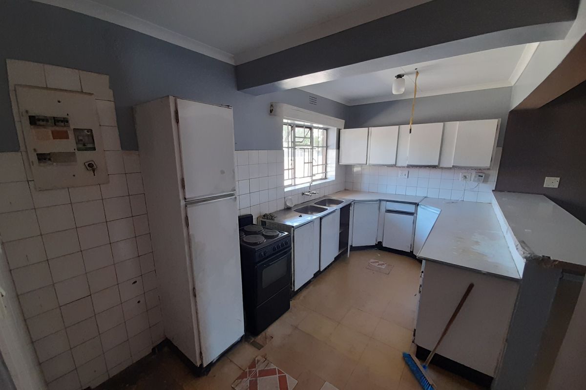 A dated kitchen featuring original cabinetry, a double sink, and tiled splashbacks, requiring modernization and cosmetic updates to improve functionality and aesthetic appeal.