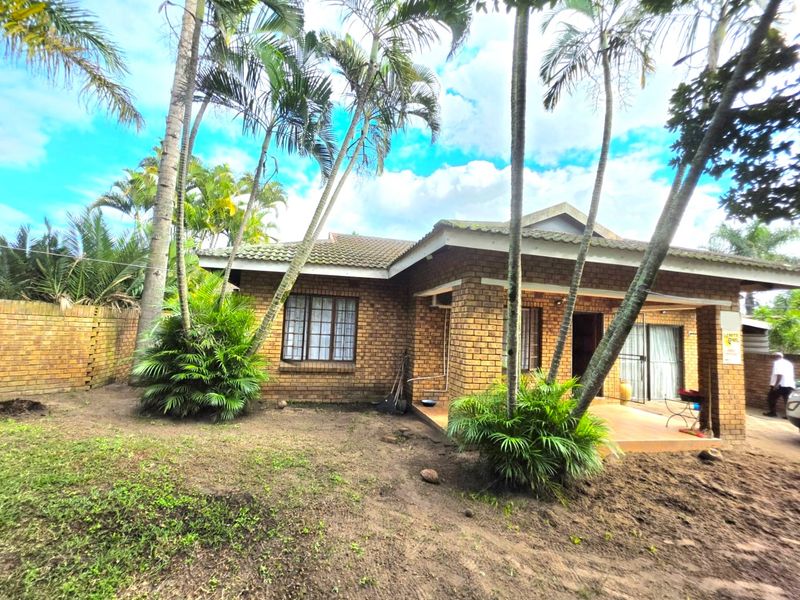 Rear view of a face brick duet property featuring a covered patio, tiled roof, and established garden area.