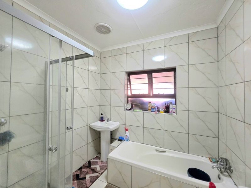 A functional bathroom featuring a pedestal basin, a built-in bathtub, and a separate glass-enclosed shower with neutral wall tiling.