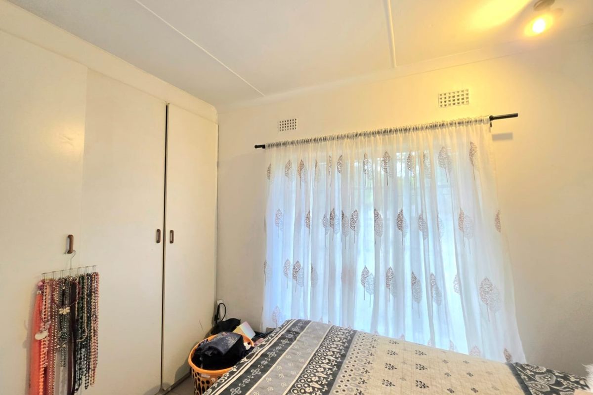 A bedroom featuring built-in cupboards and natural light through a window with curtaining.