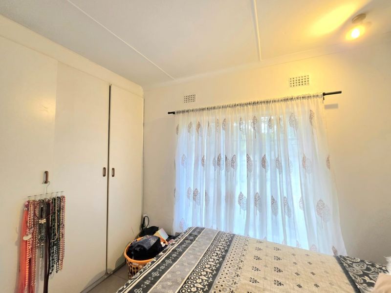 A bedroom featuring built-in cupboards and natural light through a window with curtaining.