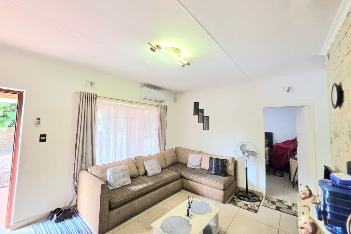 A comfortable living room featuring tiled flooring, an exposed brick wall, and an integrated air conditioning unit with direct access to the outdoor area.