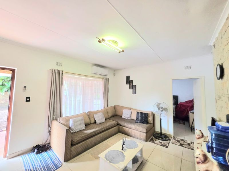 A comfortable living room featuring tiled flooring, an exposed brick wall, and an integrated air conditioning unit with direct access to the outdoor area.