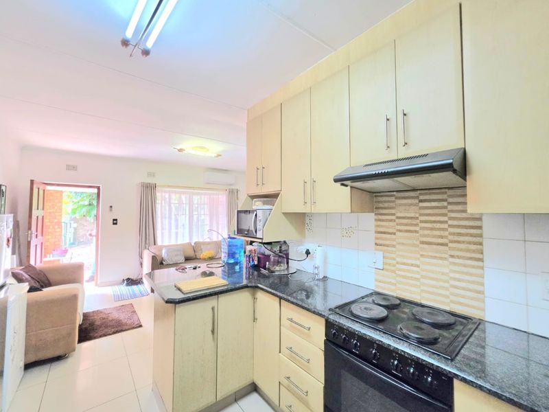 Open-plan kitchen featuring light-toned cabinetry, granite countertops, and integrated appliances, flowing into a comfortable living area with direct access to the exterior.