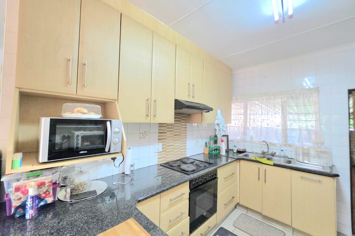Functional kitchen featuring light wood cabinetry, granite countertops, built-in electric hob, oven, extractor fan, and a double sink with tiled backsplash.