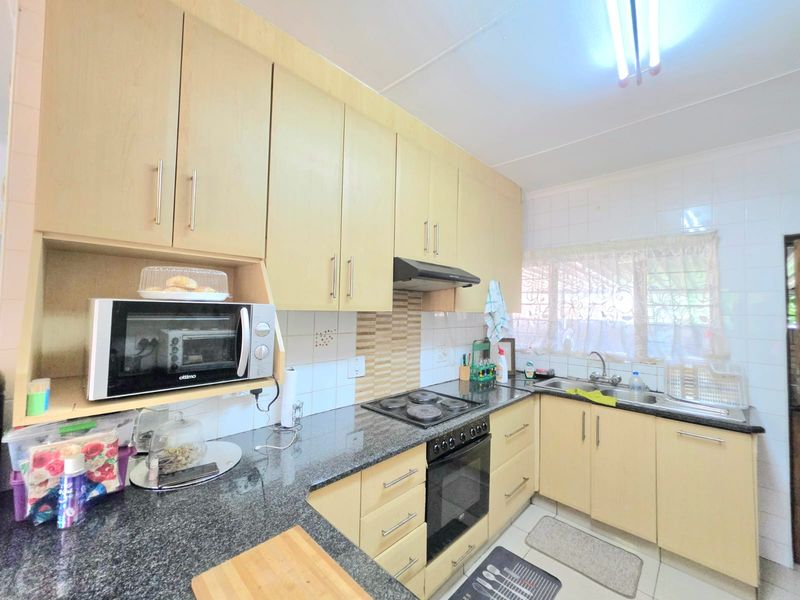 Functional kitchen featuring light wood cabinetry, granite countertops, built-in electric hob, oven, extractor fan, and a double sink with tiled backsplash.