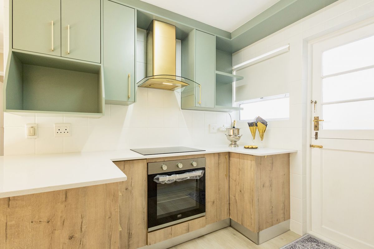 Modern kitchen featuring sage green upper cabinetry, wood-look lower cabinets, integrated appliances, and a clean tiled backsplash with direct exterior access.