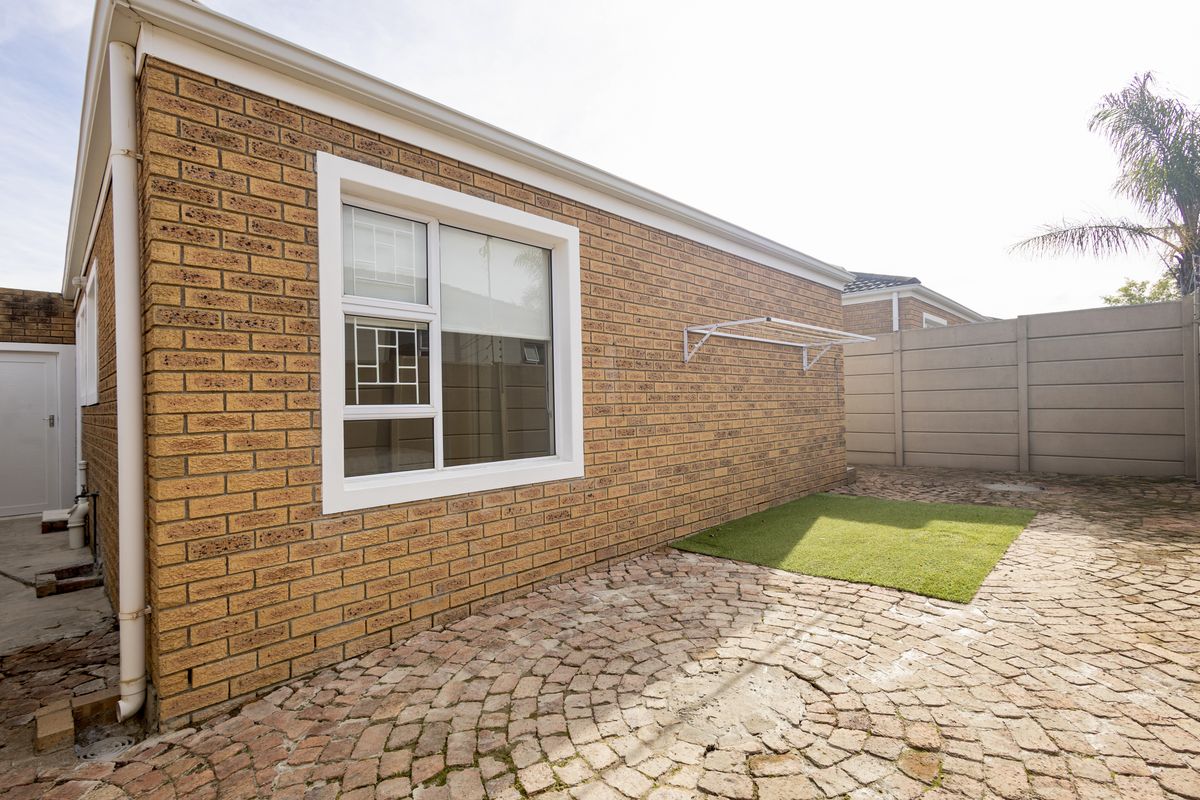 A well-maintained rear exterior featuring face brick walls, cobblestone paving, a small artificial grass patch, and a wall-mounted clothesline.