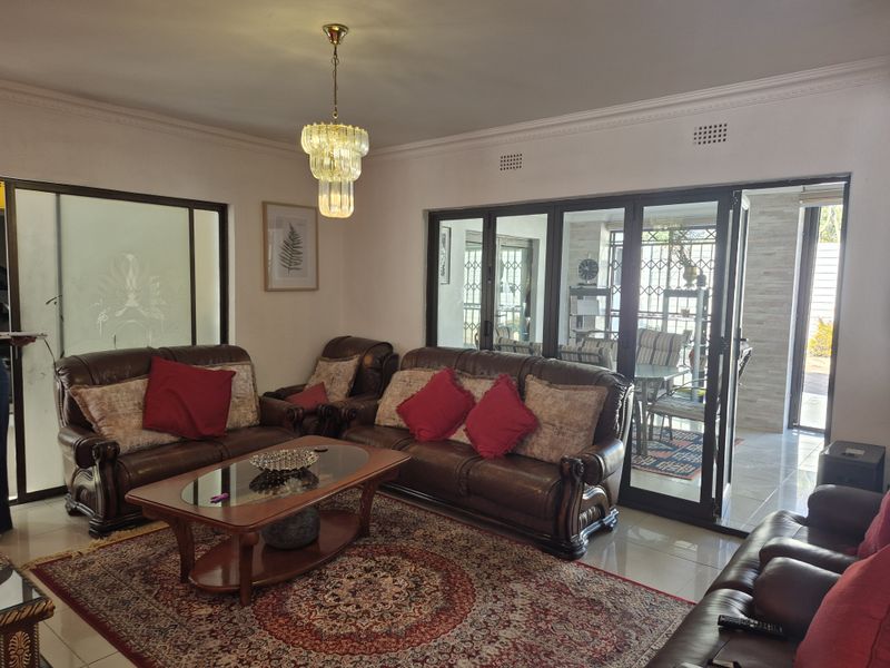 Spacious living room featuring elegant crown molding, a crystal chandelier, and large bi-fold glass doors that provide seamless access to the outdoor patio area.