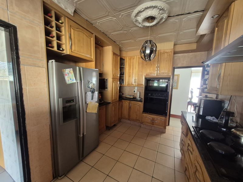 A functional kitchen featuring wooden cabinetry, built-in appliances, tiled flooring, and decorative ceiling tiles, offering a traditional layout with ample storage space.