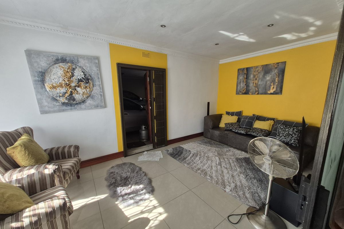 A living room featuring tiled flooring, recessed downlighting, and decorative cornicing, with a folding door leading to an adjacent space.
