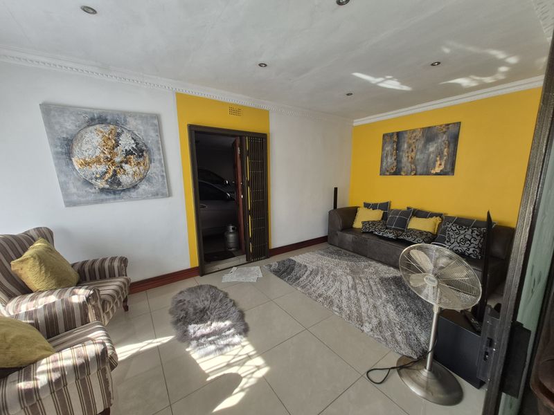 A living room featuring tiled flooring, recessed downlighting, and decorative cornicing, with a folding door leading to an adjacent space.