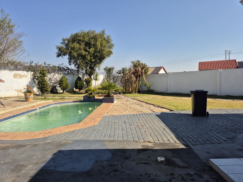 Outdoor pool area featuring a swimming pool, paved patio space, and a surrounding boundary wall with a lawn area.