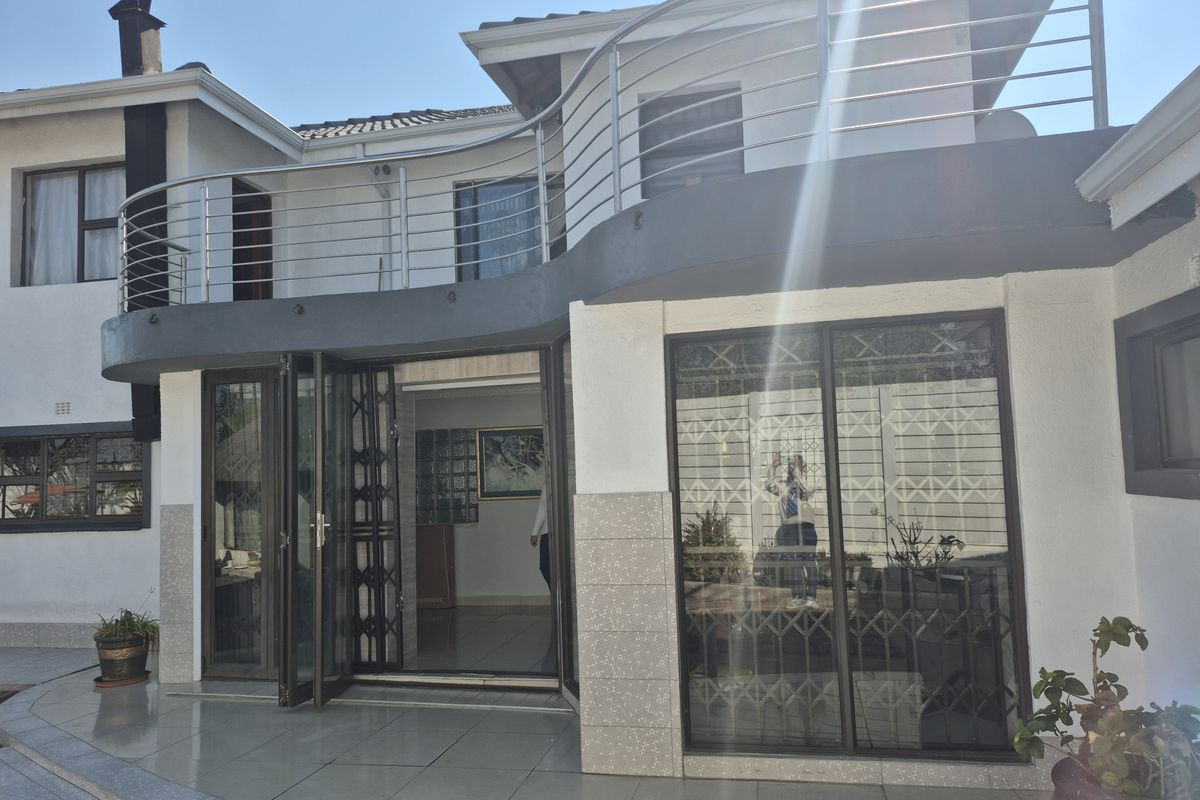 Rear exterior view featuring a tiled patio, sliding glass doors with security gates, and an upper-level balcony with stainless steel railings.