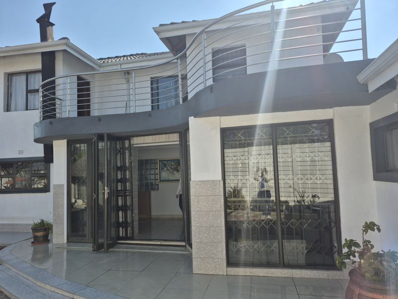 Rear exterior view featuring a tiled patio, sliding glass doors with security gates, and an upper-level balcony with stainless steel railings.
