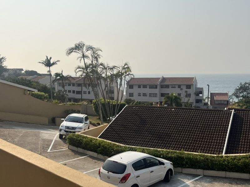 An elevated view overlooking a residential complex parking area with a distant ocean horizon.