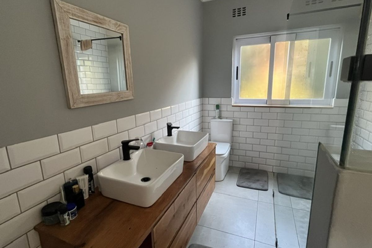 Modern bathroom featuring a double vanity with vessel sinks, subway tile backsplash, a glass shower enclosure, and a toilet.