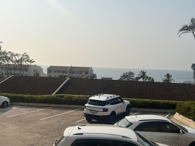 An elevated view overlooking a parking area with a distant ocean horizon and coastal residential buildings.