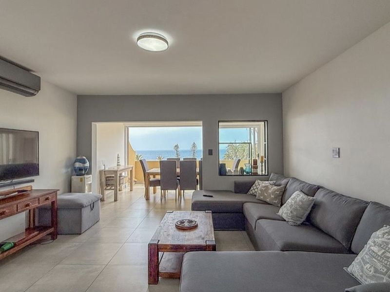 Spacious open-plan living area featuring tiled floors, a wall-mounted air conditioner, and seamless access to a balcony with ocean views.