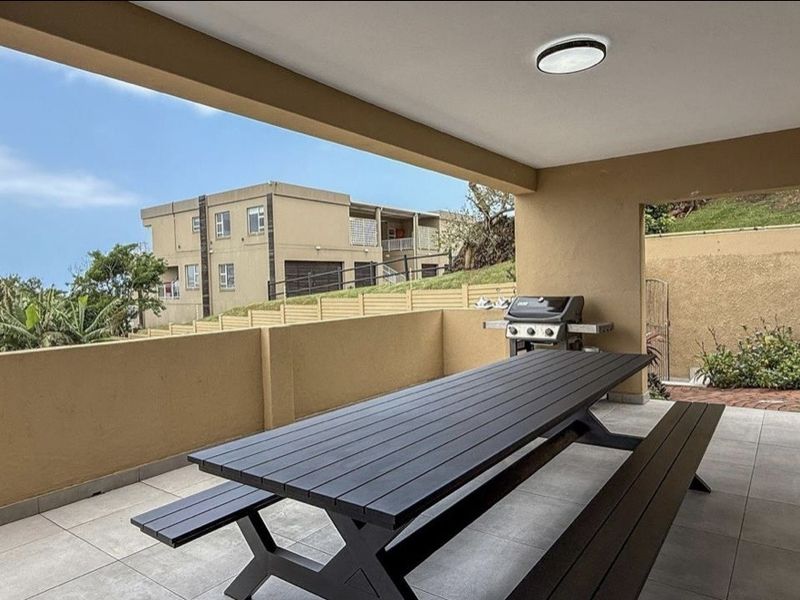 A spacious covered patio featuring tiled flooring, a low masonry wall, and direct access to the interior through sliding glass doors.