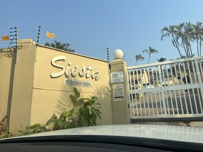 Front entrance view of Siesta apartment complex at 76 Ocean Drive, featuring a secure gated access point and boundary wall with electric fencing.