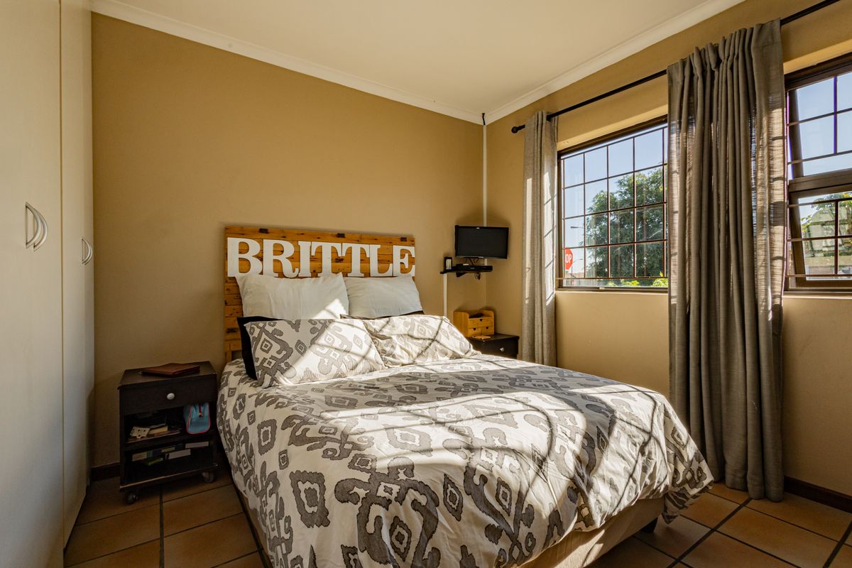 A functional bedroom featuring tiled flooring, a built-in wardrobe, and a window fitted with security bars.
