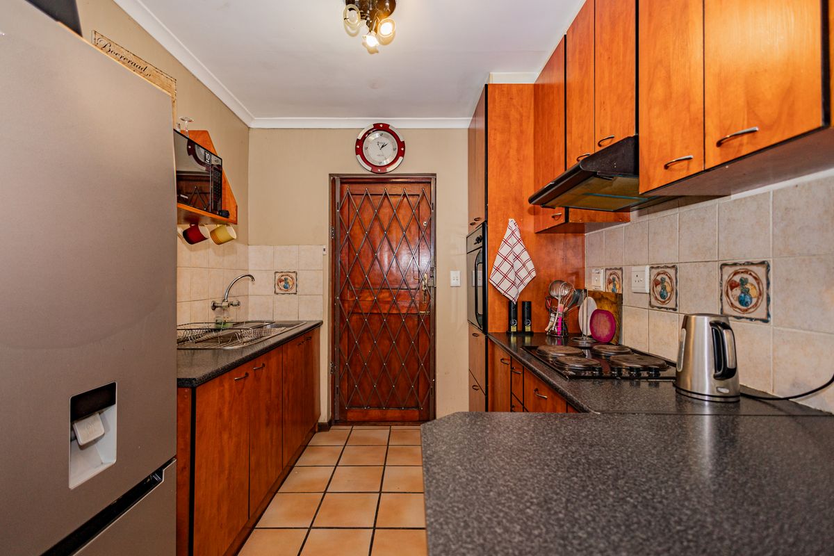 A functional kitchen featuring wooden cabinetry, dark laminate countertops, built-in oven and hob, tiled backsplash, and tiled flooring with a security door.