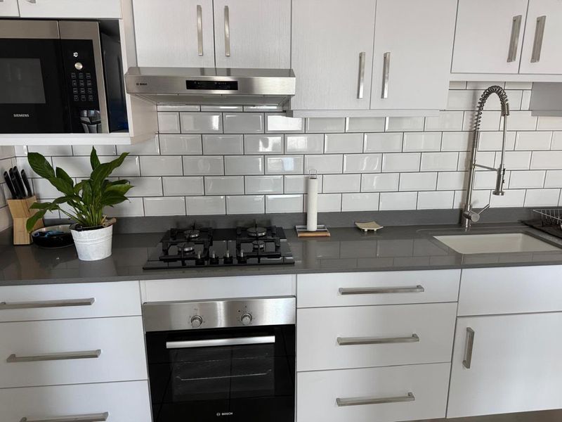 Modern kitchen featuring white cabinetry, quartz countertops, subway tile backsplash, and integrated Bosch appliances including a gas hob, oven, and microwave.