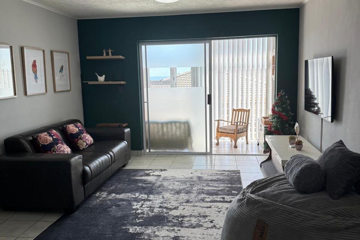 A well-maintained living room featuring tiled flooring, a dark accent wall, floating shelves, and a sliding glass door leading to a balcony.