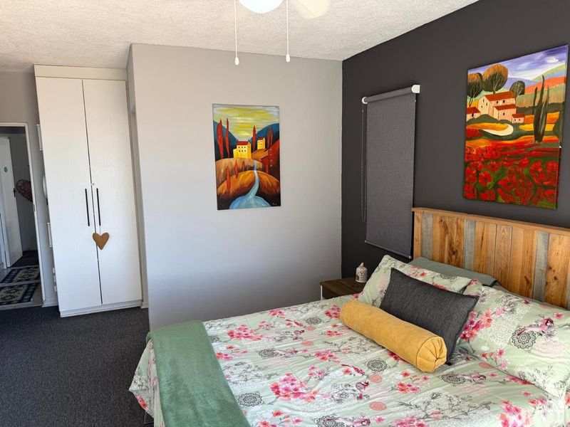 A well-maintained bedroom featuring a built-in wardrobe, ceiling fan, and a modern dark accent wall.