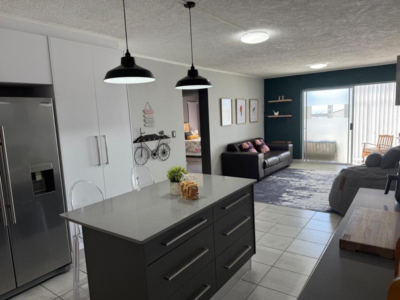 Modern open-plan living area featuring a central kitchen island with quartz countertops, sleek cabinetry, and seamless flow to a bright patio through sliding doors.