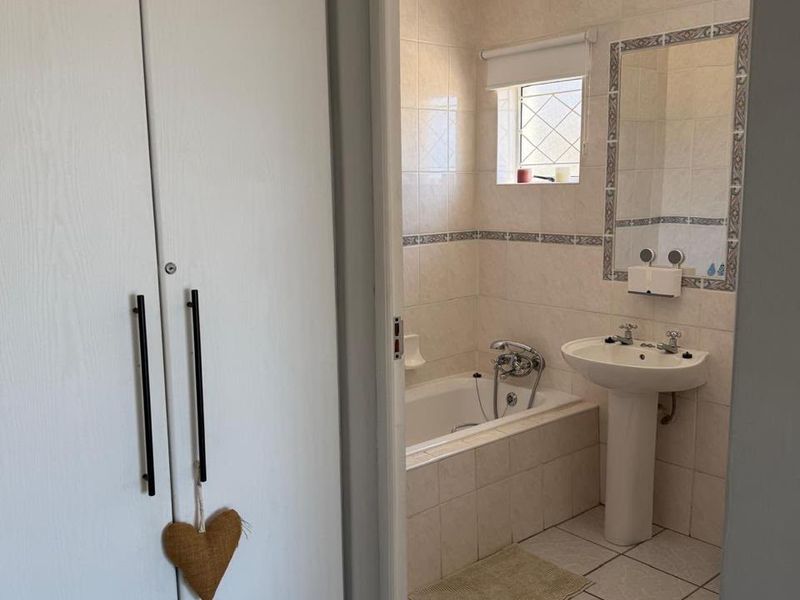A functional bathroom featuring a bathtub, pedestal basin, and tiled finishes, accessed via a hallway with built-in storage cupboards.