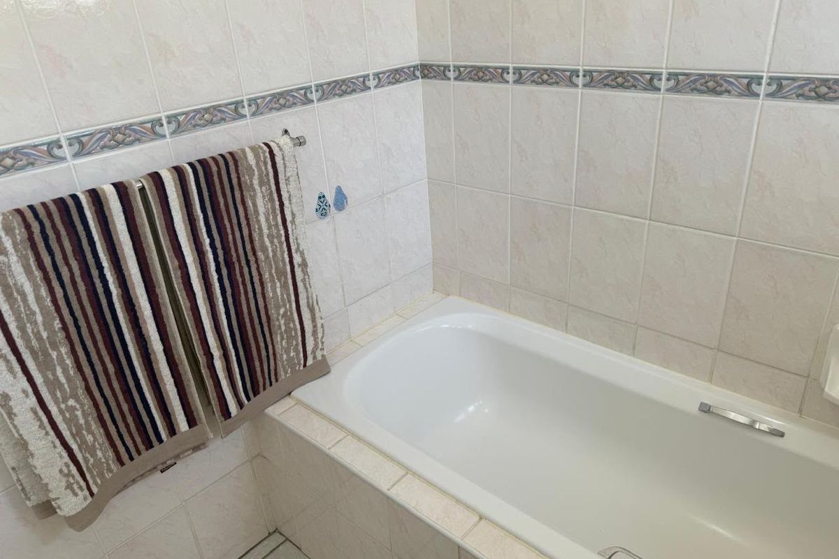 A functional bathroom featuring a built-in bathtub with neutral ceramic wall tiles and a decorative accent border.