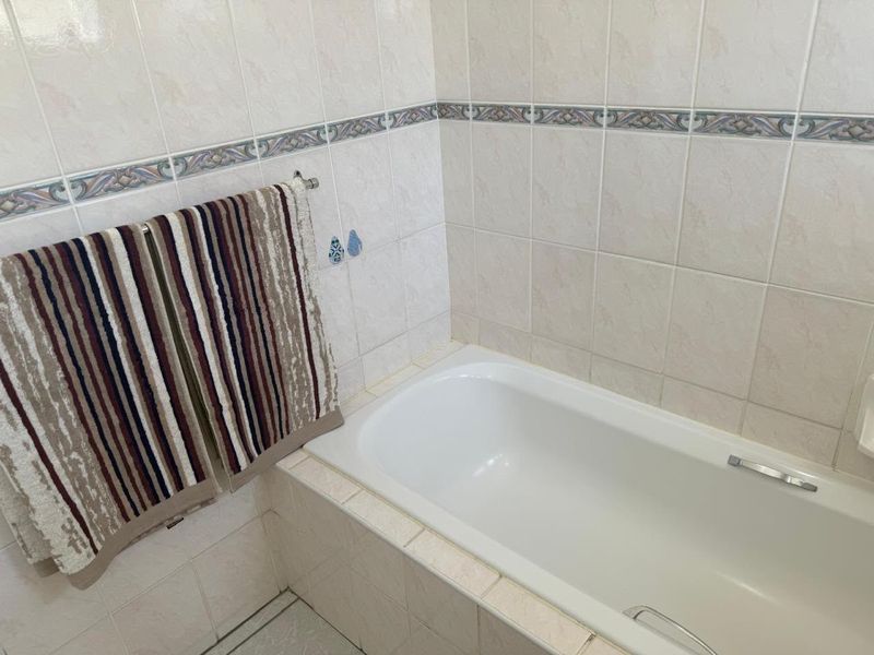 A functional bathroom featuring a built-in bathtub with neutral ceramic wall tiles and a decorative accent border.