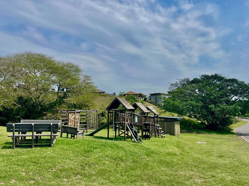 A communal garden area featuring a wooden playground structure, slide, and outdoor seating set within a landscaped residential environment.