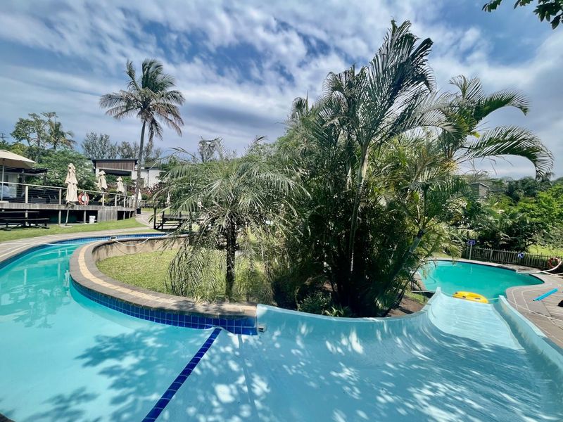 Outdoor pool area featuring a water slide, landscaped garden surroundings, and wooden decking, providing a recreational space within the residential estate.